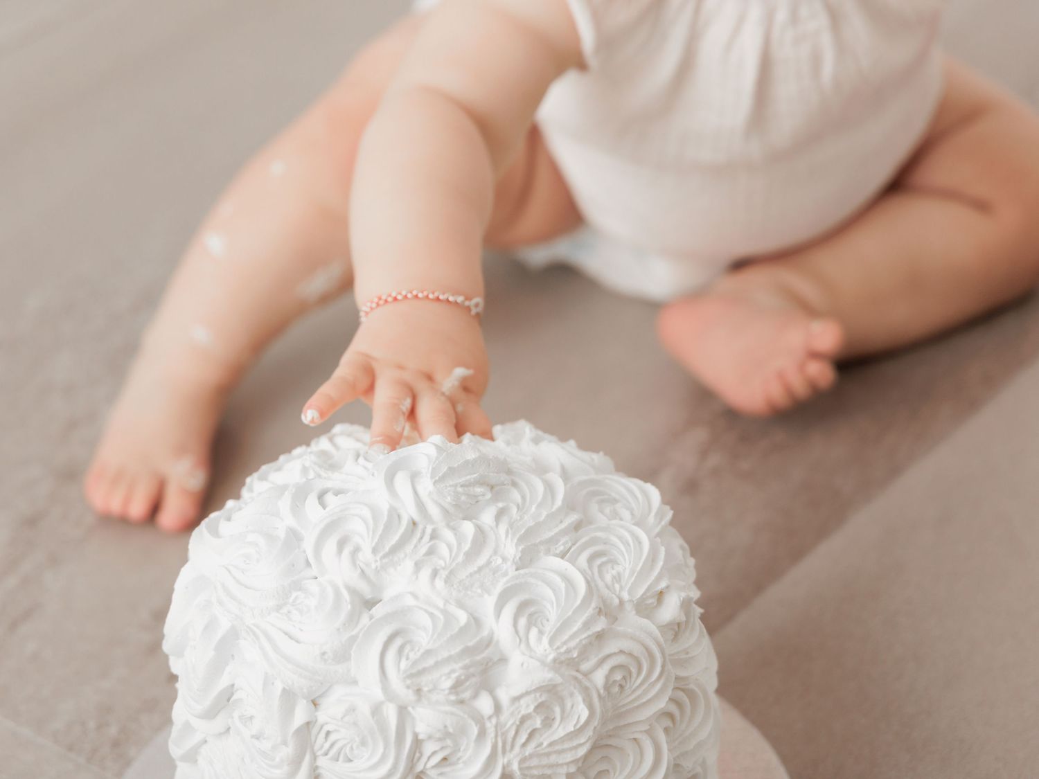 Closeup of white rosette cake details with baby's feet visible in background.