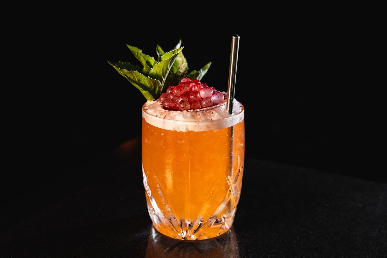 Colorful craft cocktails garnished with fresh herbs on dark background.
