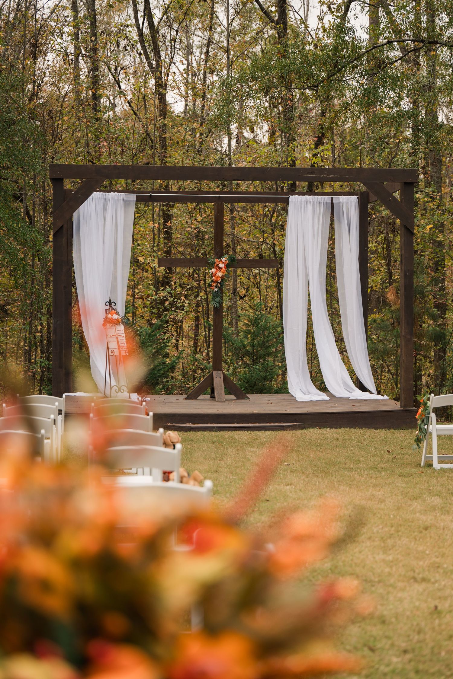Rustic wooden wedding arch with flowing white curtains set in a forest clearing, decorated with autumn flowers.