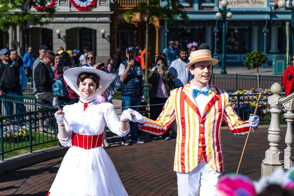 Performers in colorful vintage costumes dance and entertain visitors on Main Street at Disney theme park.