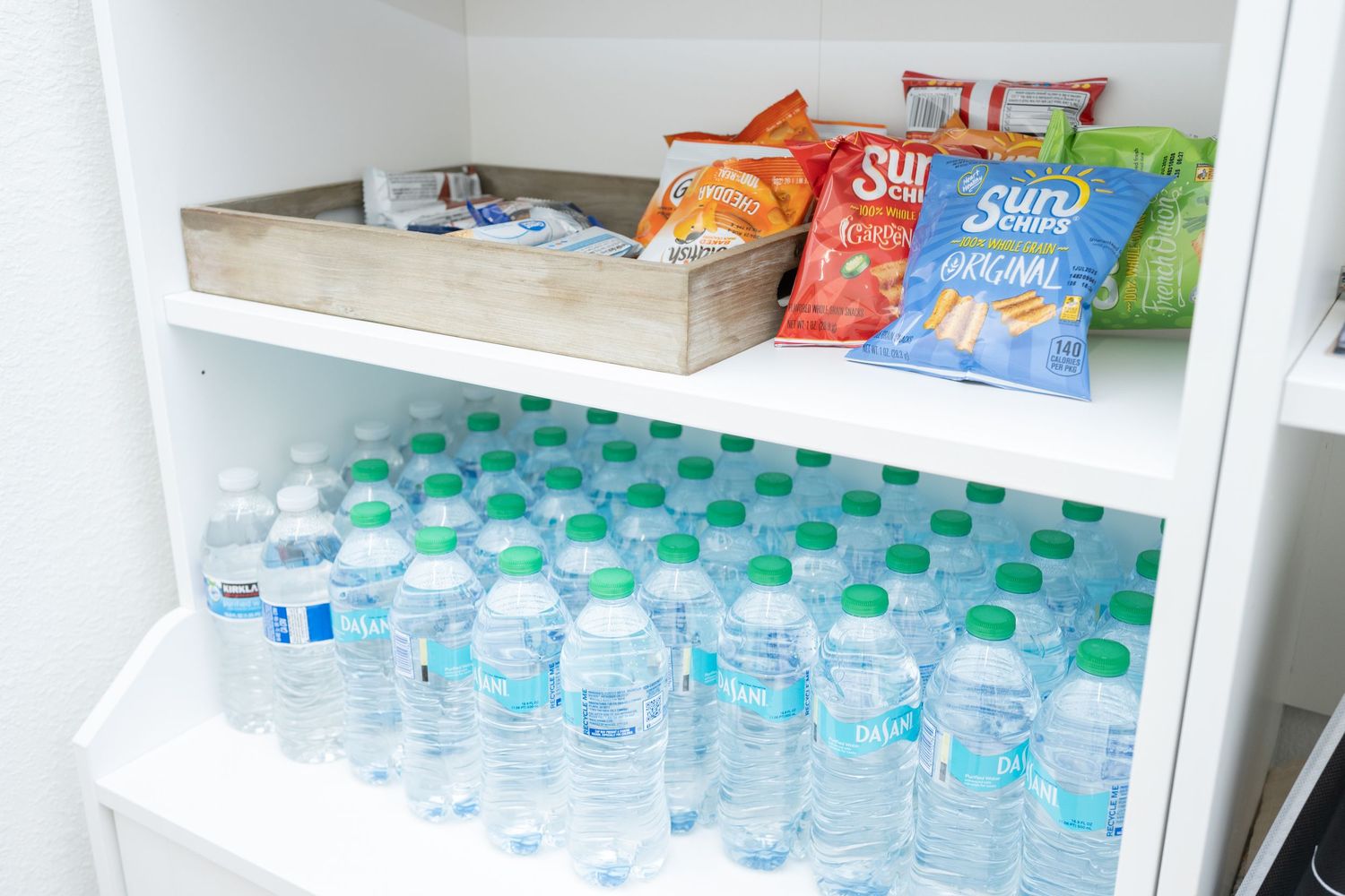 Organized pantry shelf with bottled water and snack bags.