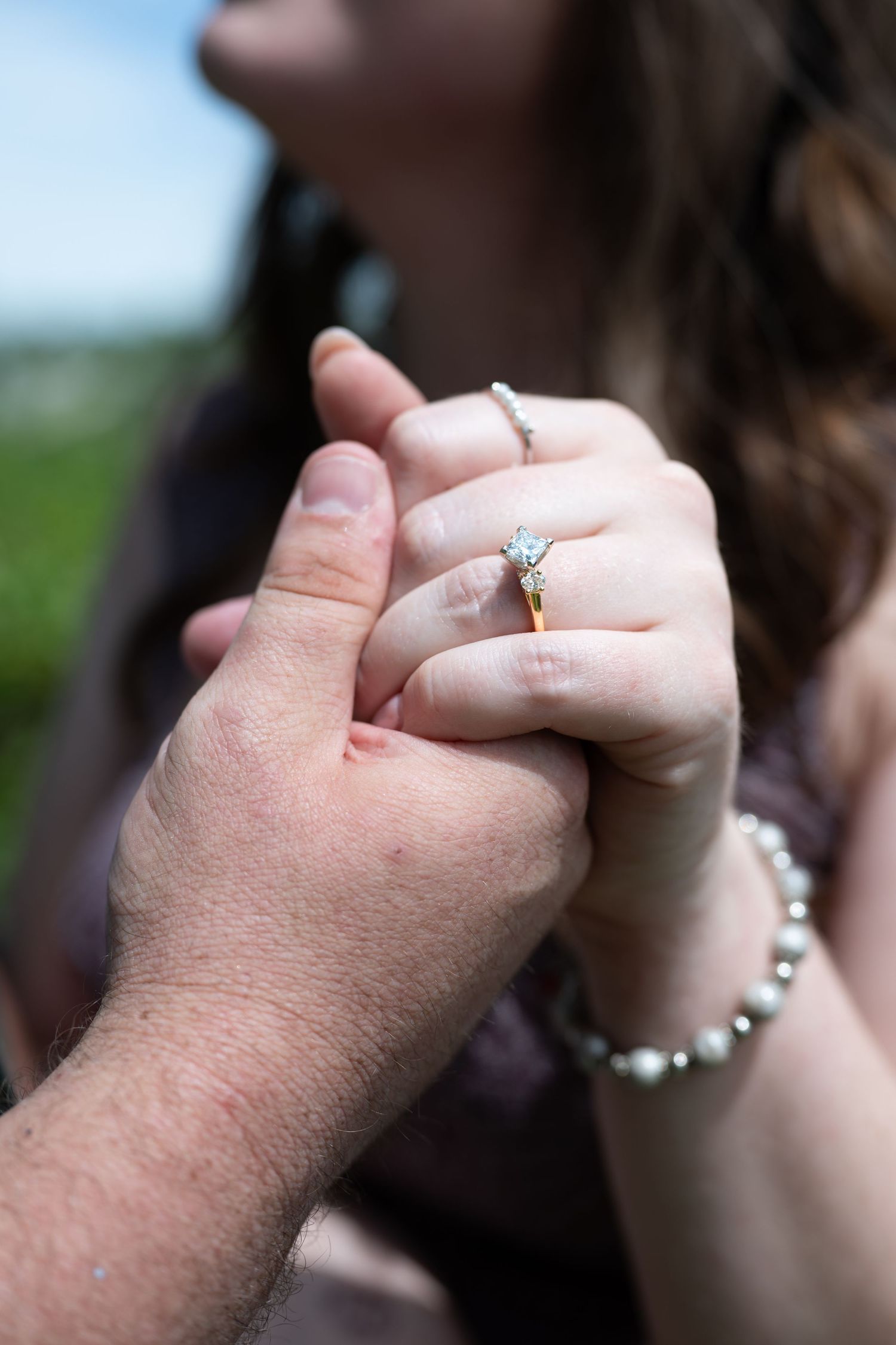 Close up shot of hands displaying elegant engagement ring with pearl bracelet.