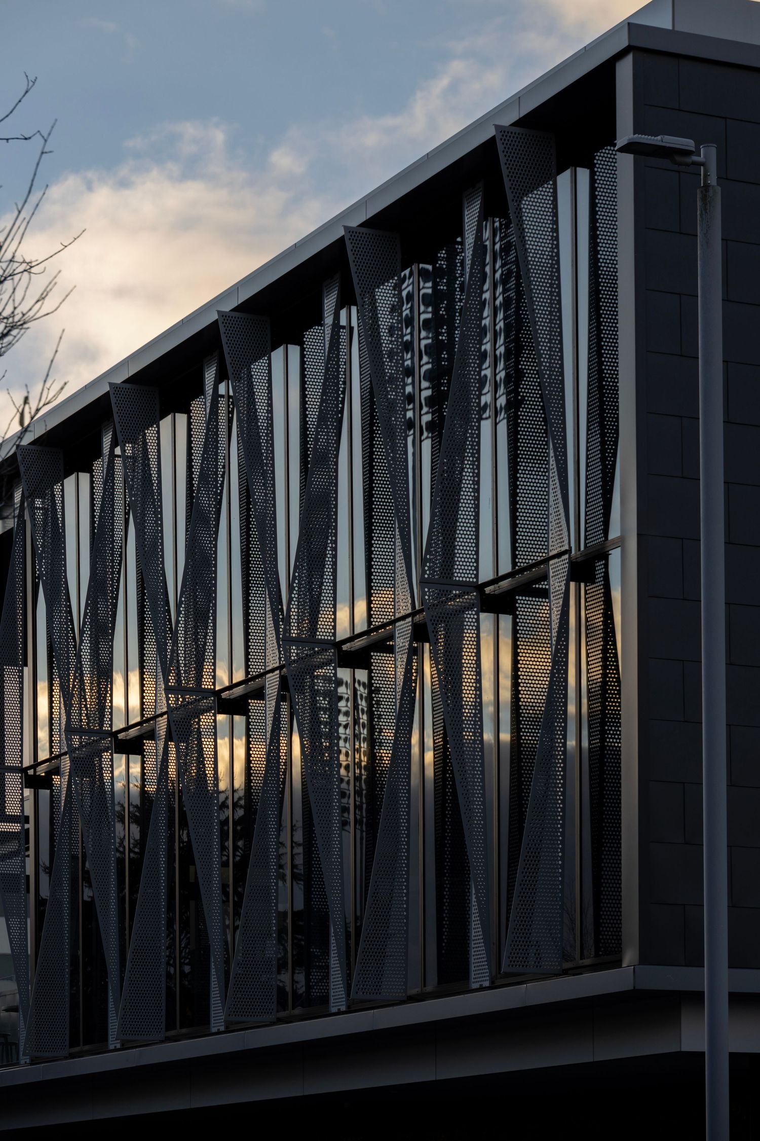 Angular metal panels cast shadows and reflections at sunset on a modern glass building exterior.