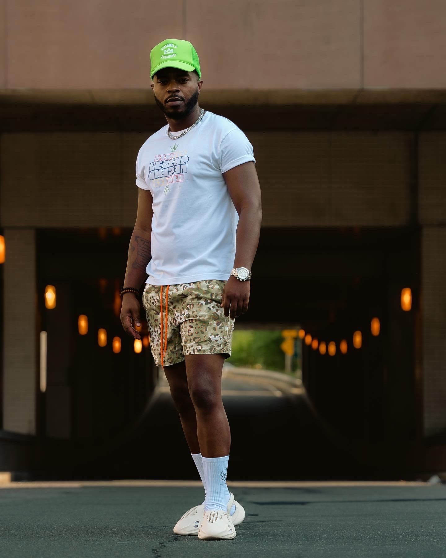 Casual summer streetwear outfit with green cap, white tee, and patterned shorts.