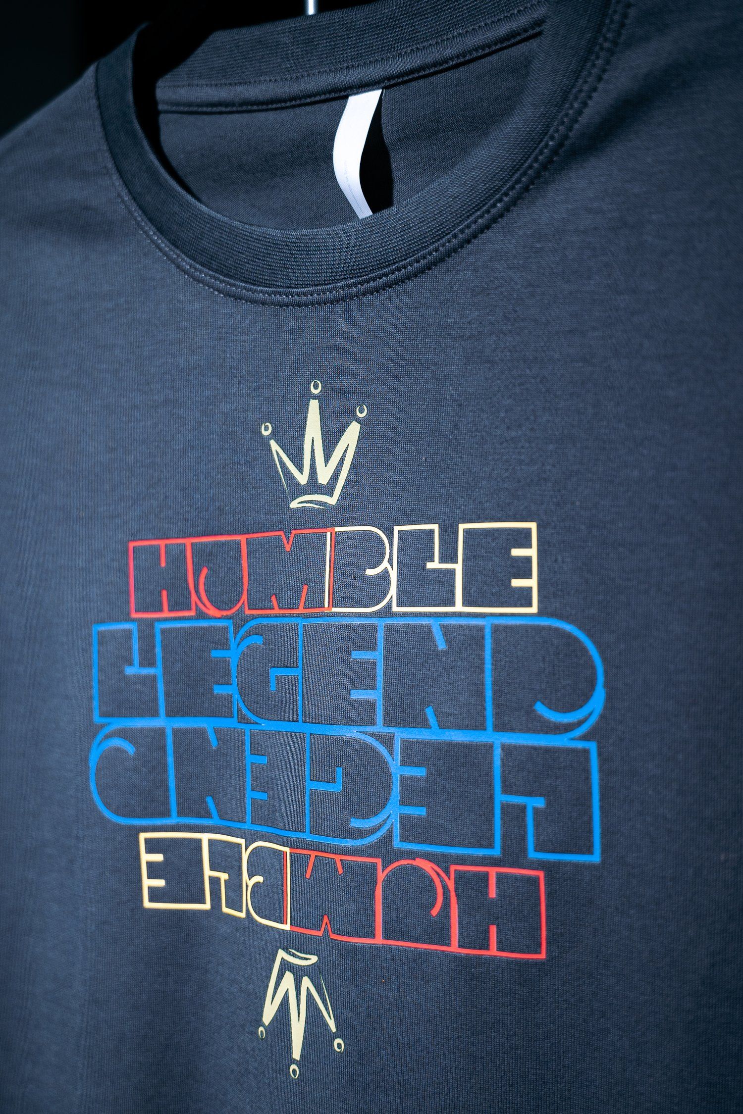 Close-up of navy t-shirt showing Humble Legend logo with crown design.