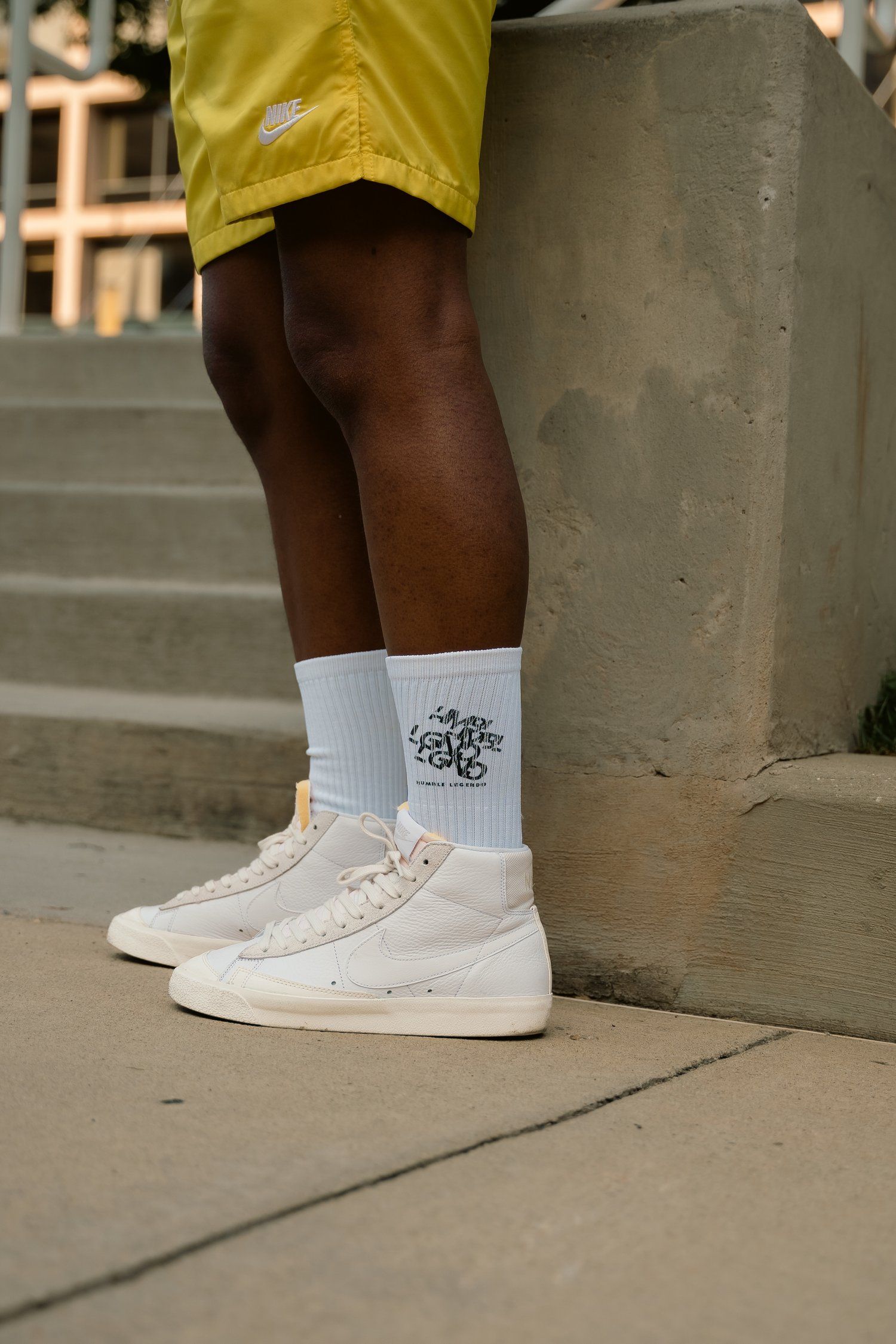 White high-top sneakers and white socks shown against concrete steps with yellow shorts visible.