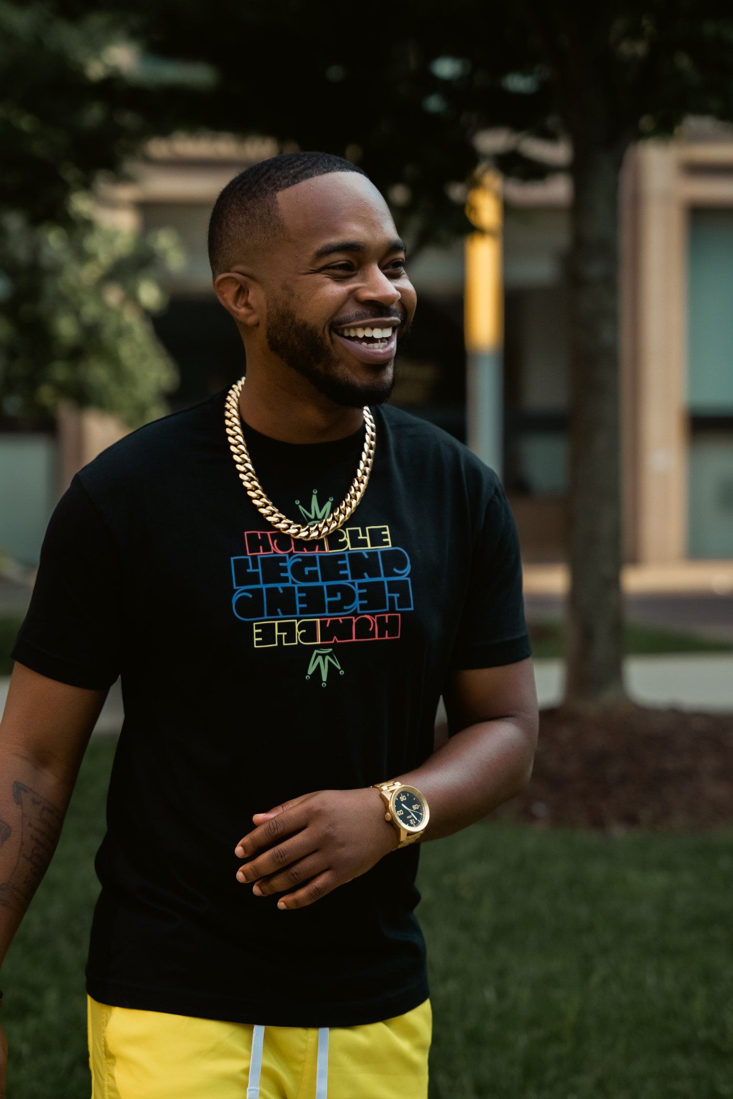 A casual outfit featuring a black t-shirt with colorful text, yellow shorts and gold chain jewelry.