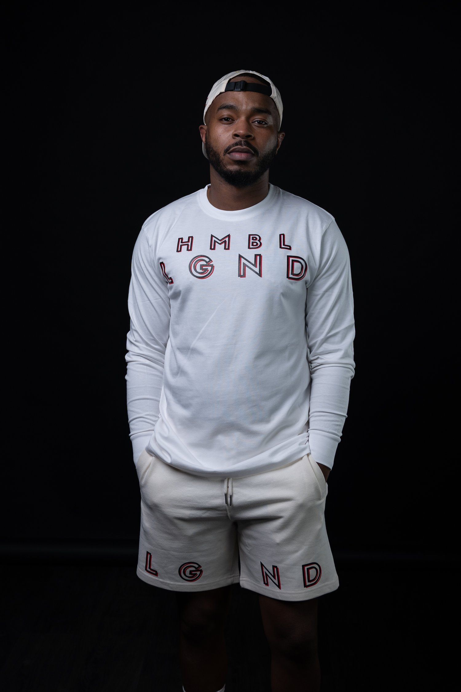 Athletic wear outfit featuring white long sleeve HMBL LGND shirt and matching shorts against dark background.