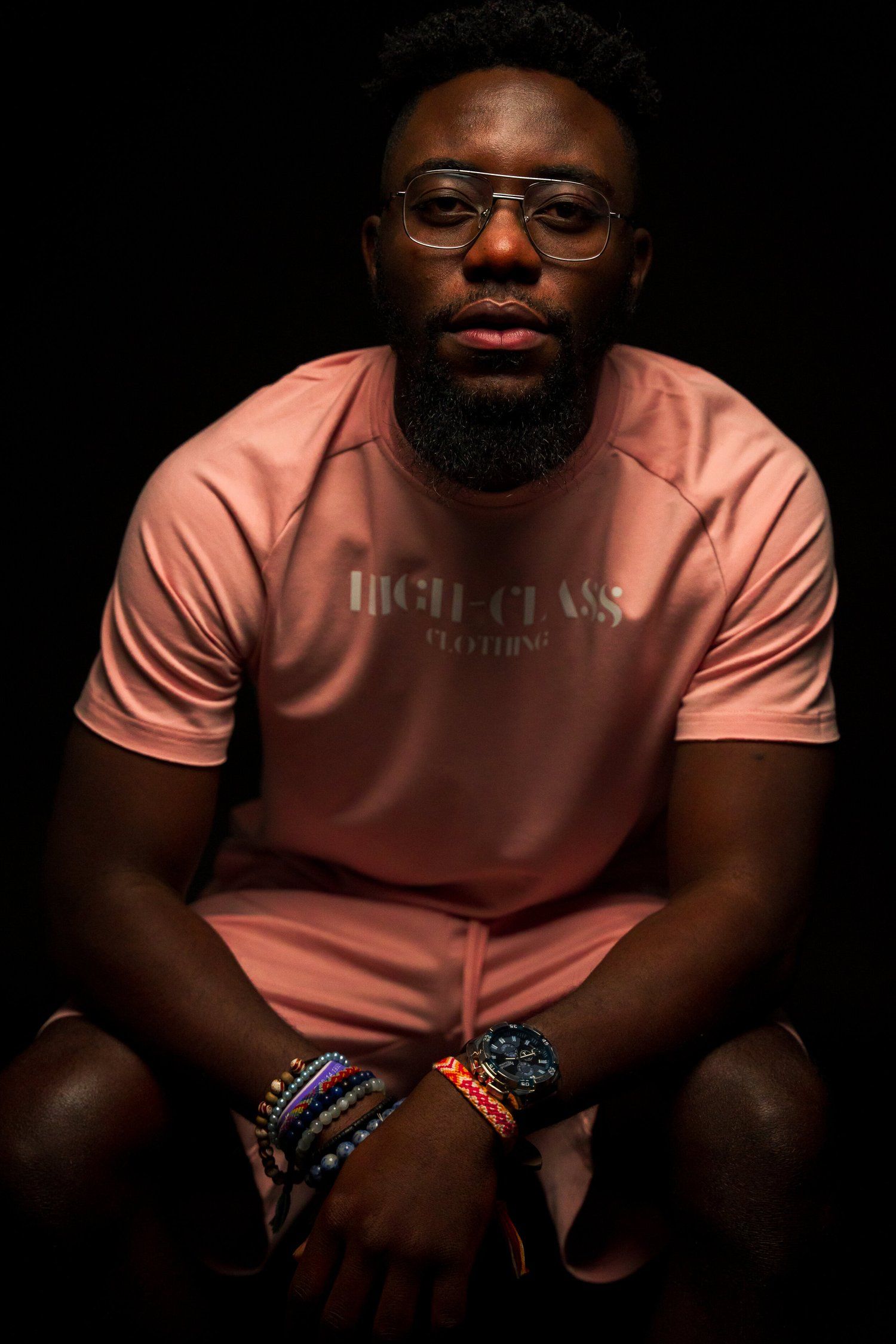 Moody portrait showing pink t-shirt and colorful beaded bracelets against dark background.