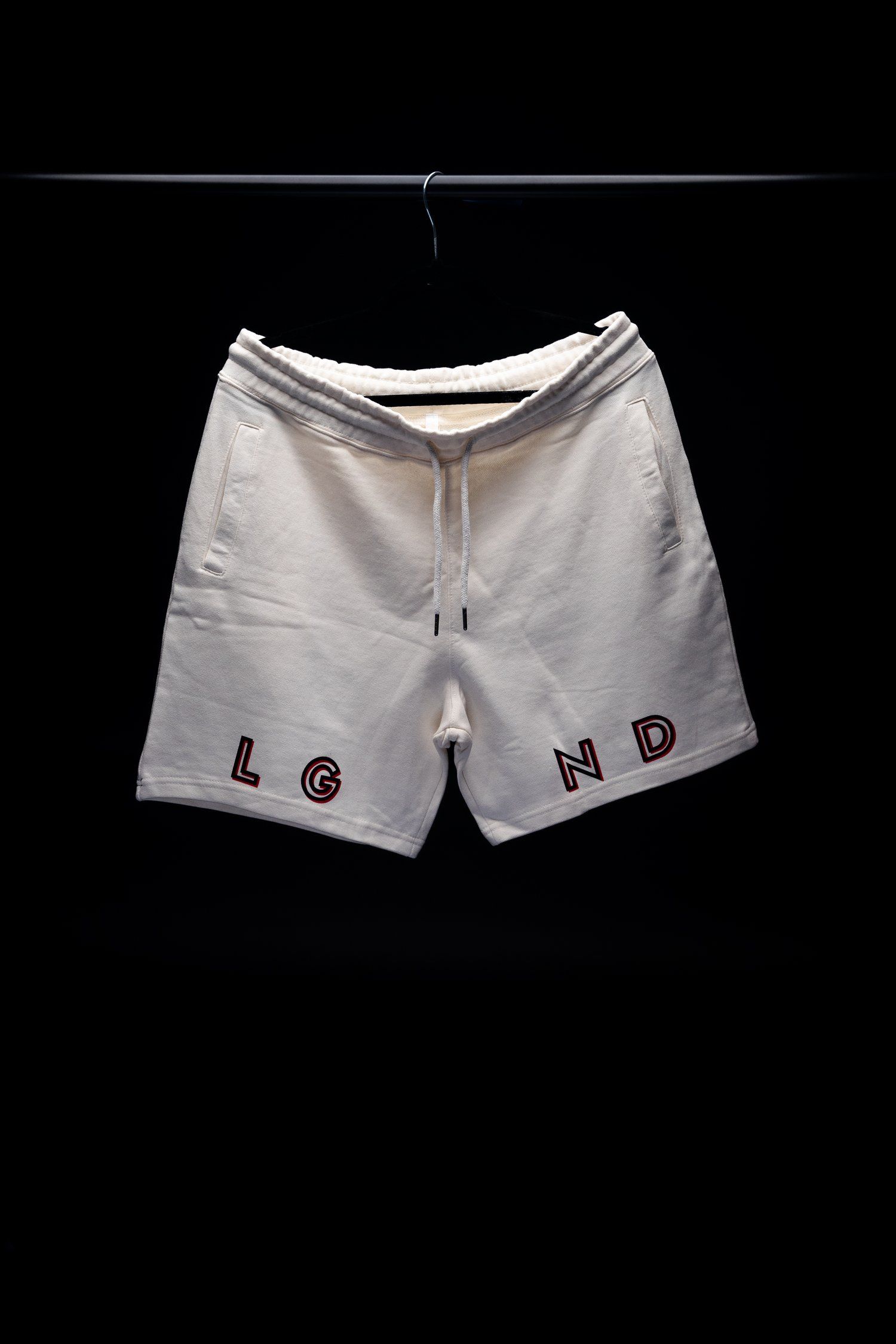 White athletic shorts with LGND text hanging against black background.