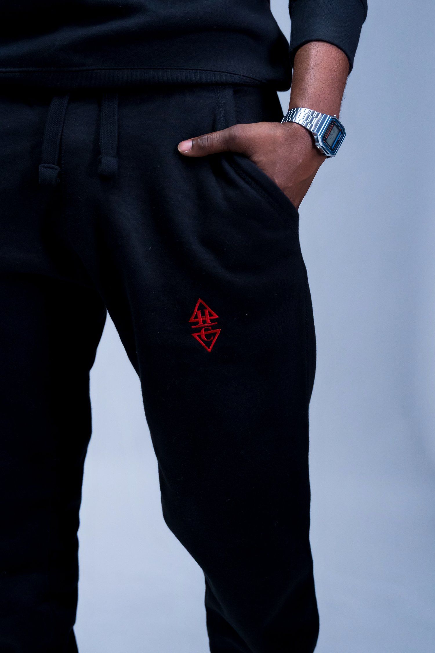Close-up of black athletic pants with red geometric logo emblem.