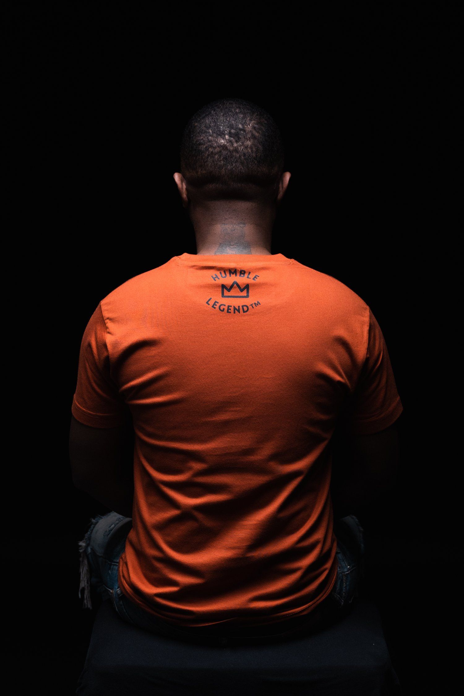 Back view of person wearing orange t-shirt with text against black background.