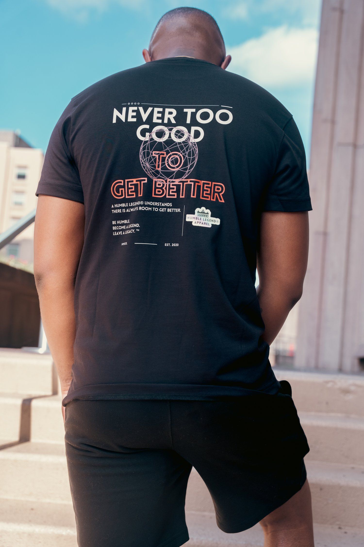 Back view of black t-shirt with motivational 'Never Too Good to Get Better' text.