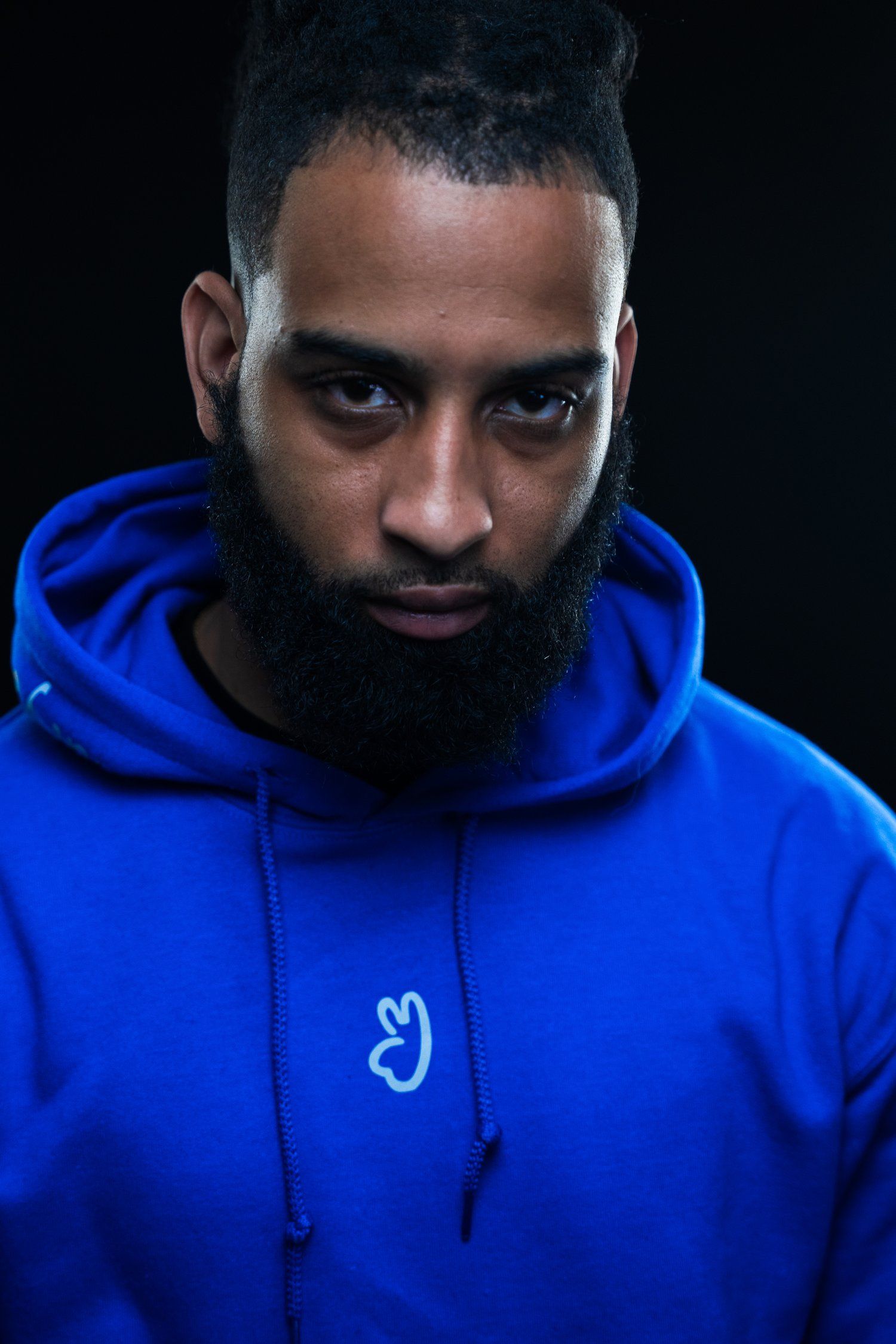 Dramatic portrait showing person in blue hoodie against dark background.