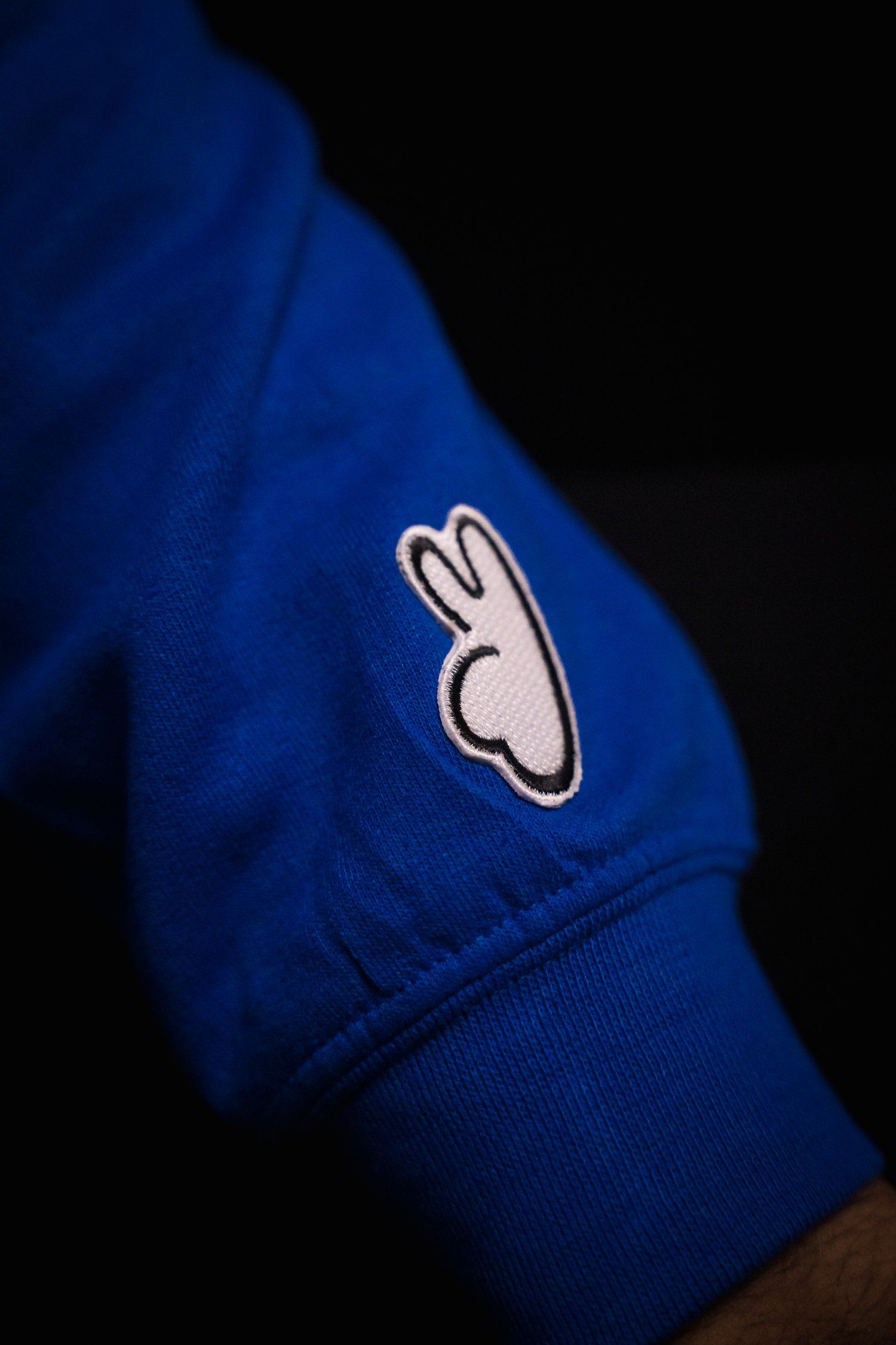 A small white bunny logo embroidered on a bright blue fabric garment.