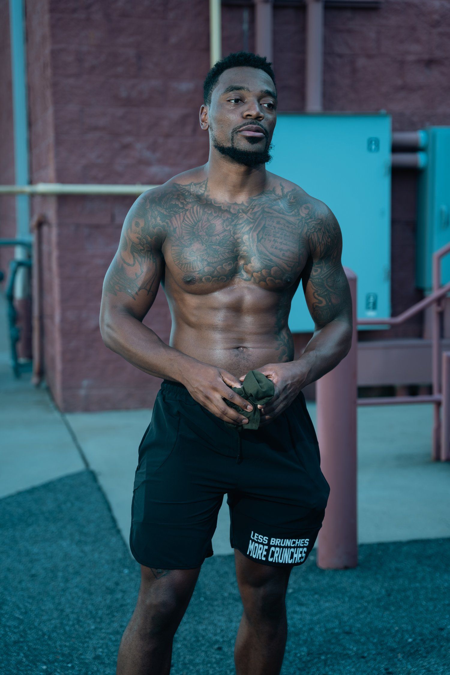 Fitness model in black shorts posing outdoors against urban background.