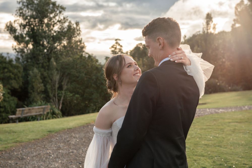 A romantic wedding moment captured during golden hour on a grassy hillside with trees in the background Cambridge New Zealand