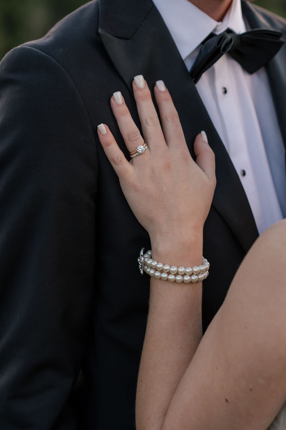 Close-up of a bride's hand with engagement ring and pearl bracelet resting on groom's tuxedo lapel Cambridge New Zealand