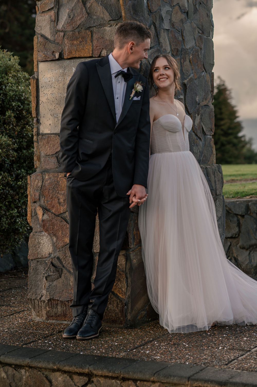 A romantic wedding portrait against a stone pillar with the couple in elegant attire Cambridge New Zealand