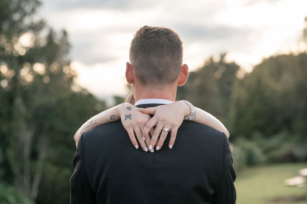 A close-up shot showing hands embracing against a black tuxedo with nature in the background Cambridge New Zealand