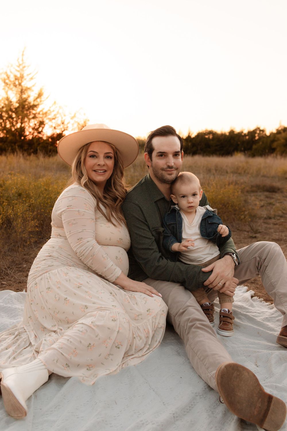 Family sits on blanket during sunset photoshoot in rustic outdoor setting.