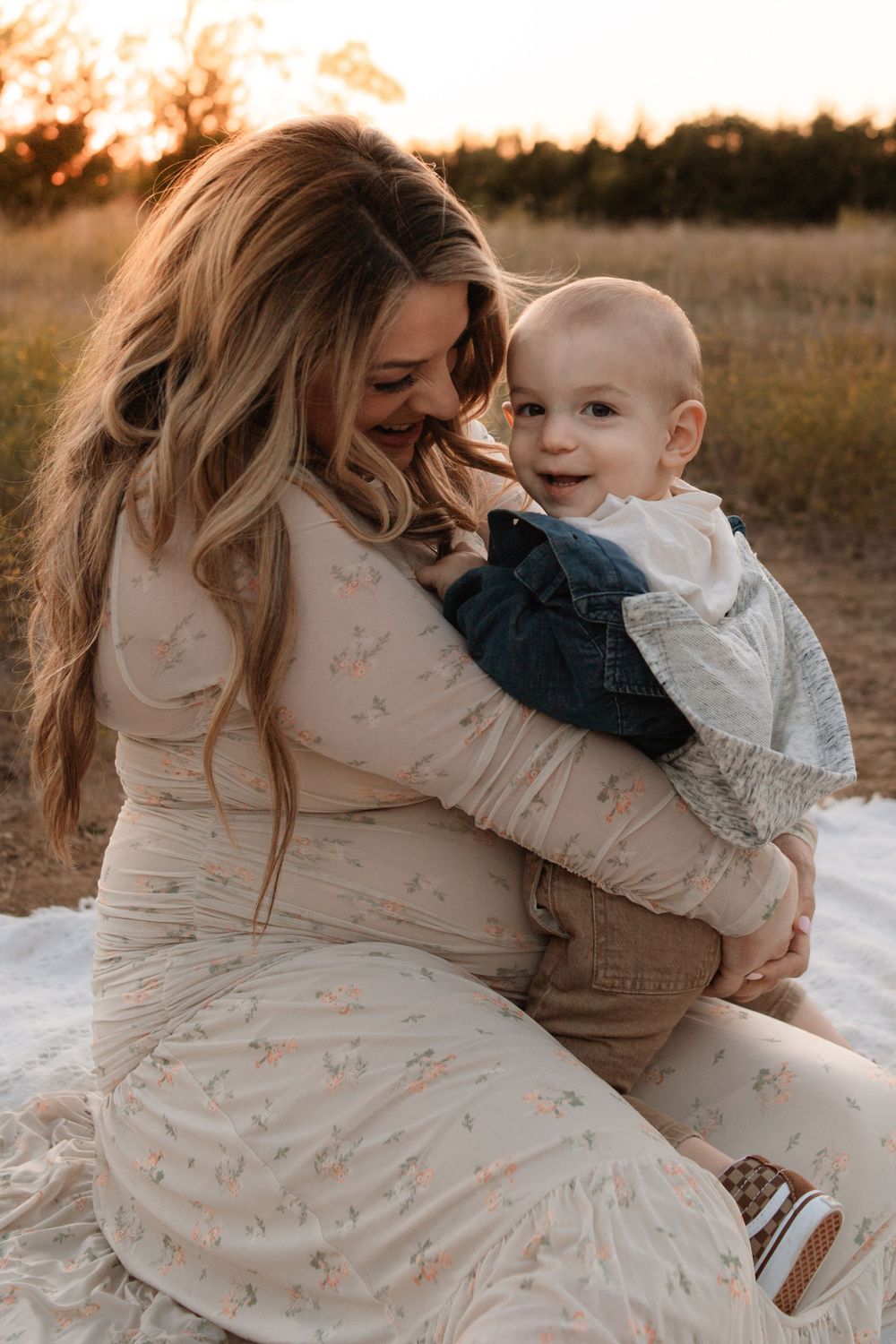 Mother and baby share joyful moment during outdoor maternity photoshoot at sunset.