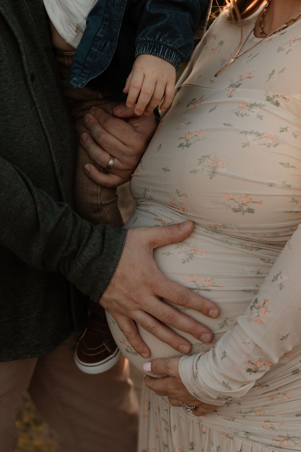 Close-up of hands tenderly resting on a pregnant belly in a floral dress.