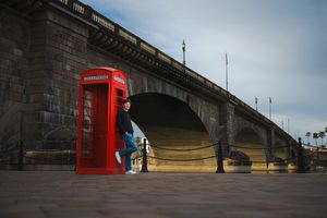 A panoramic view of a red British phone booth against a stone bridge with dramatic cloudy sky in Lake Havasu at the London Bridge.