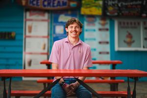 A person in a pink shirt smiles while sitting at a red picnic table outside an ice cream shop. Senior portrait photography by Dusty Wooddell