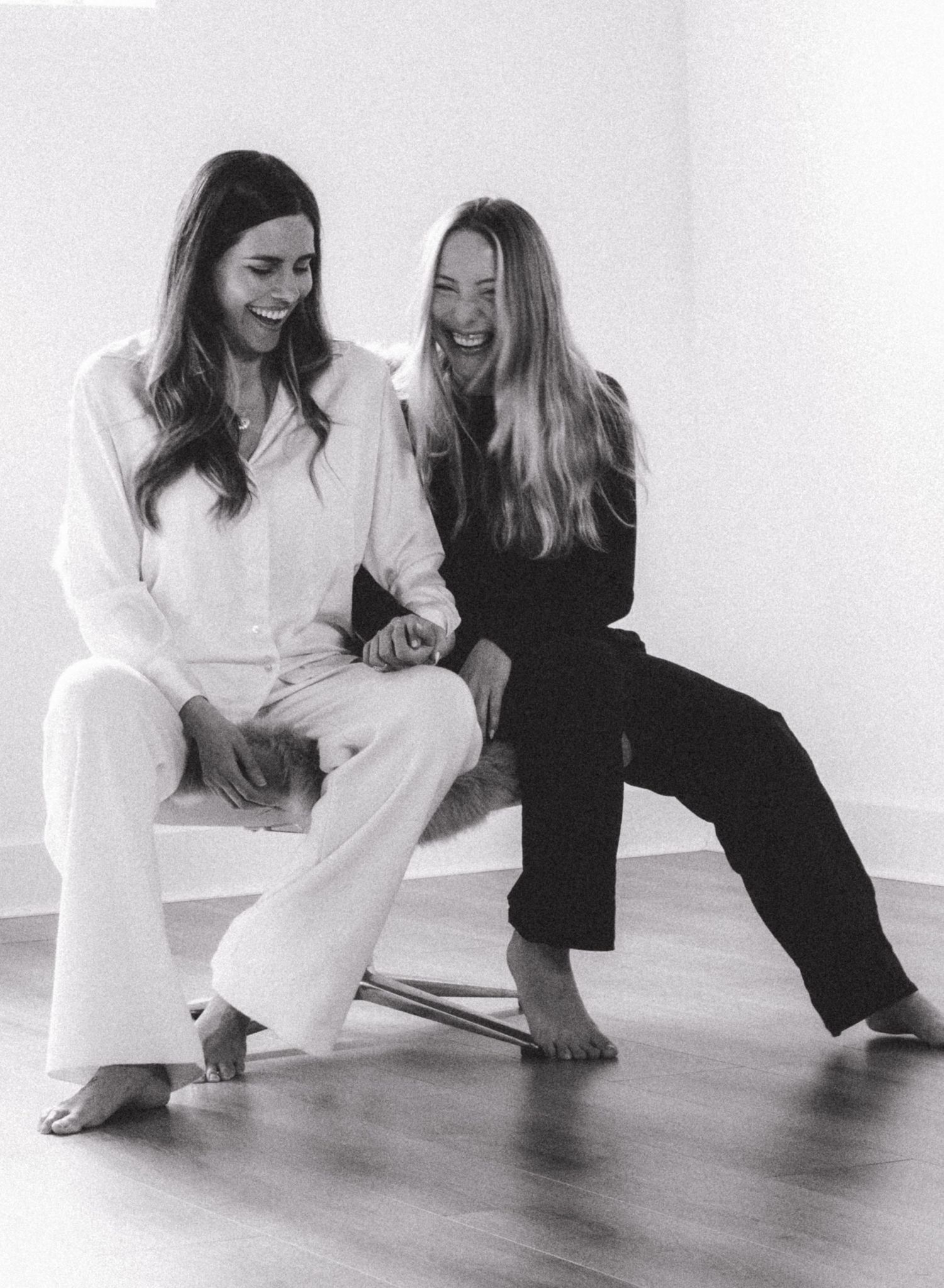 Models seated on floor share lighthearted moment in black and white contrasting outfits.