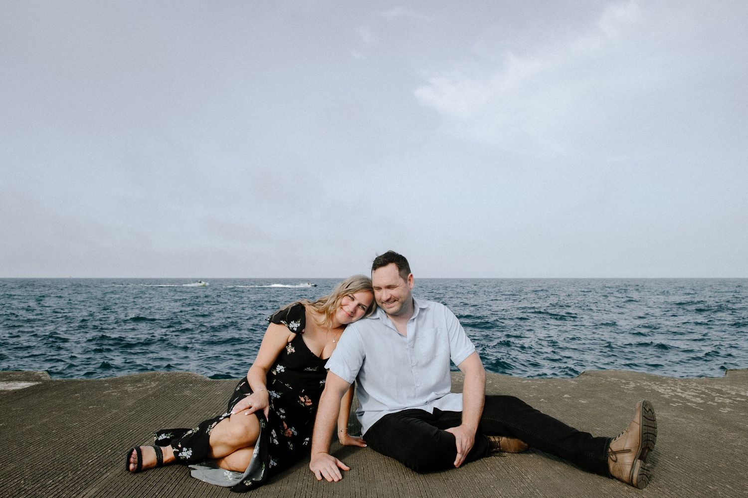 A scenic photoshoot by the ocean showing a couple posing together on rocks and sand during golden hour.