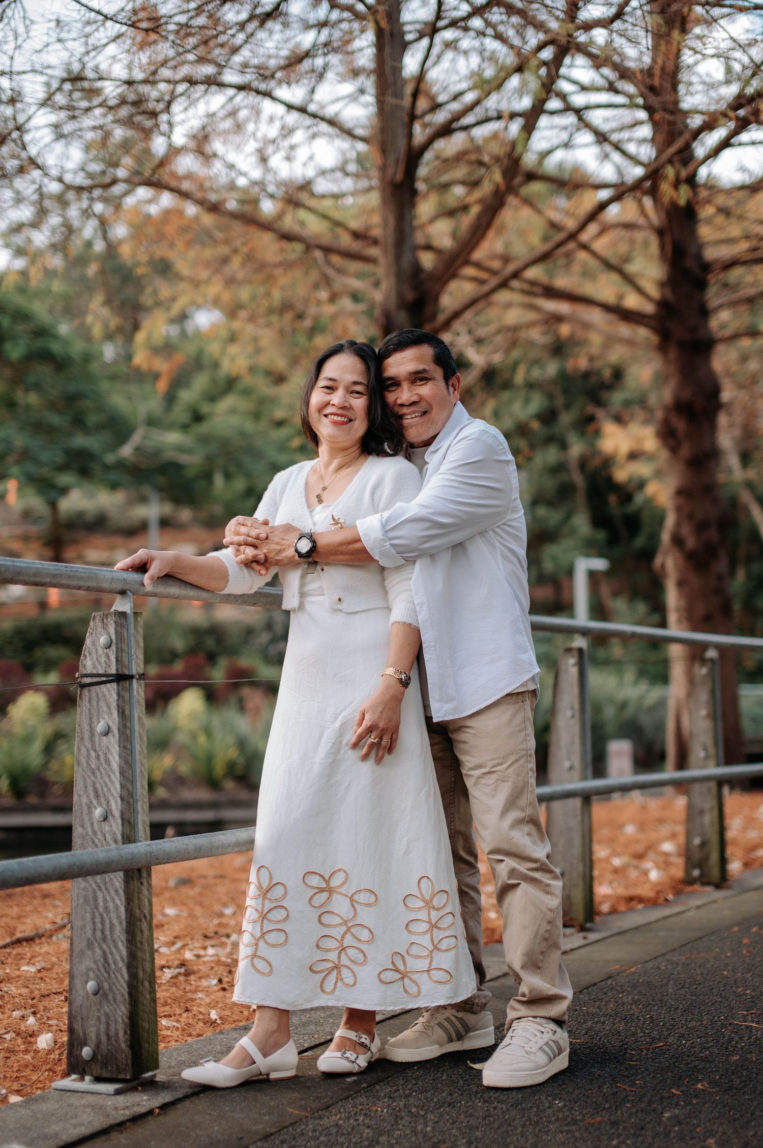 A romantic couple poses together on a wooden bridge surrounded by autumn trees.