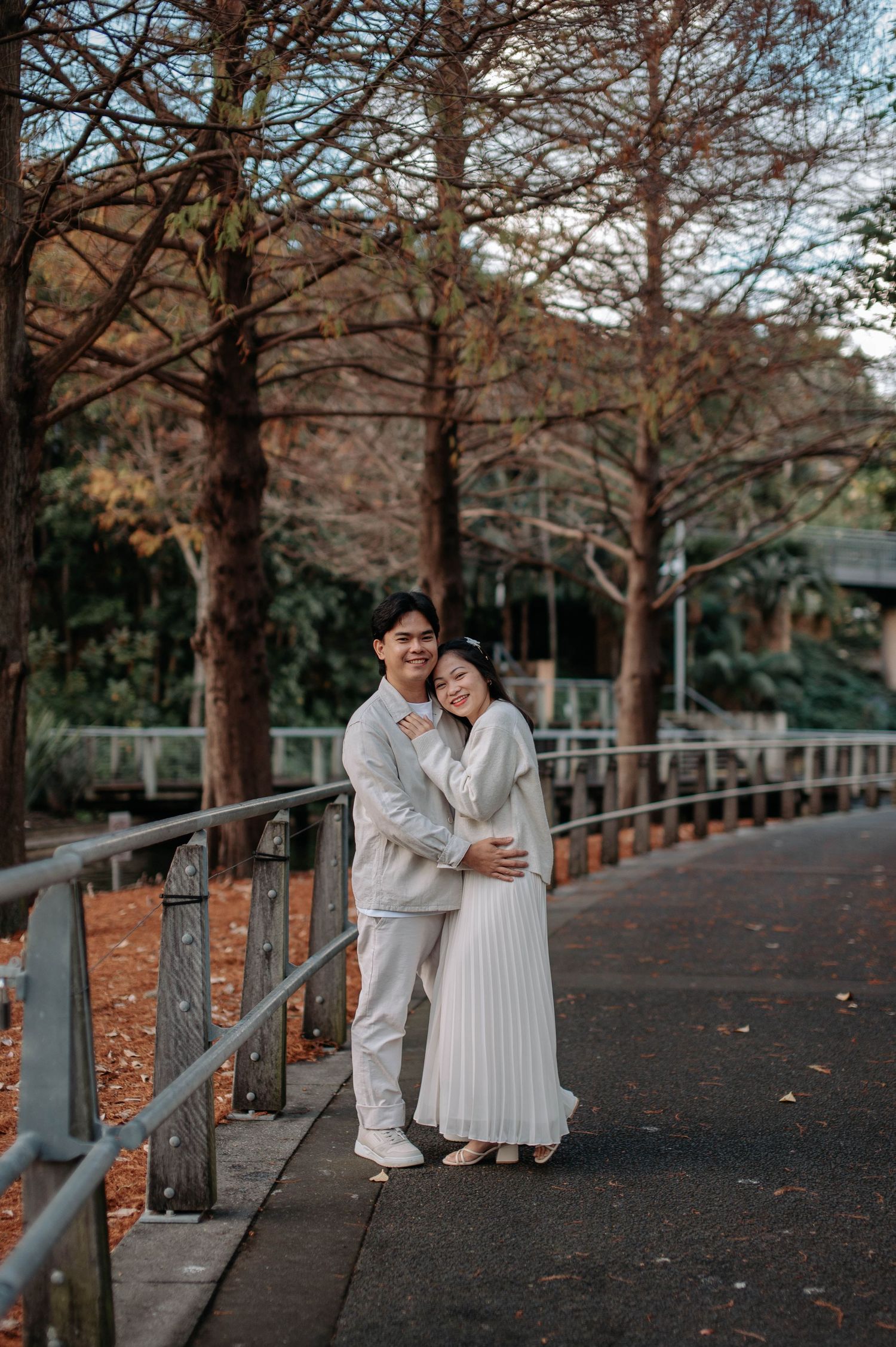 A couple shares a romantic moment on a tree-lined path with autumn leaves on the ground.