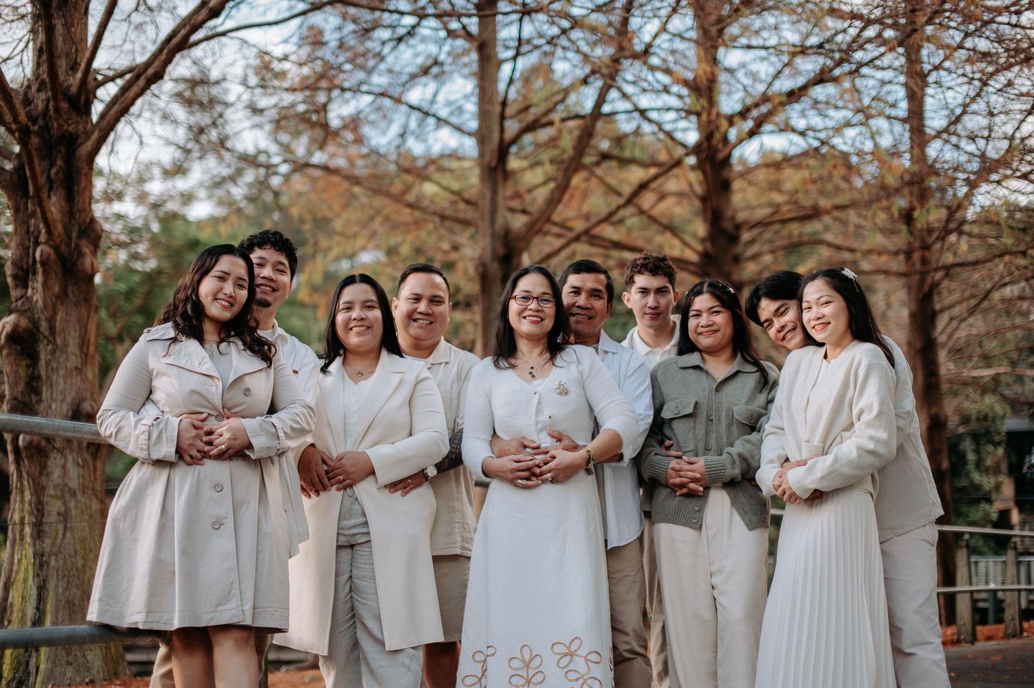 Group wearing matching white and beige outfits pose together during outdoor autumn photoshoot at park.