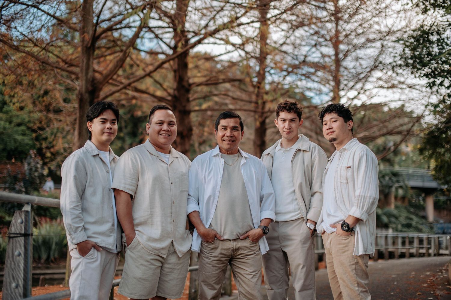 Group wearing coordinated light colored outfits poses casually outdoors in autumn scenery.