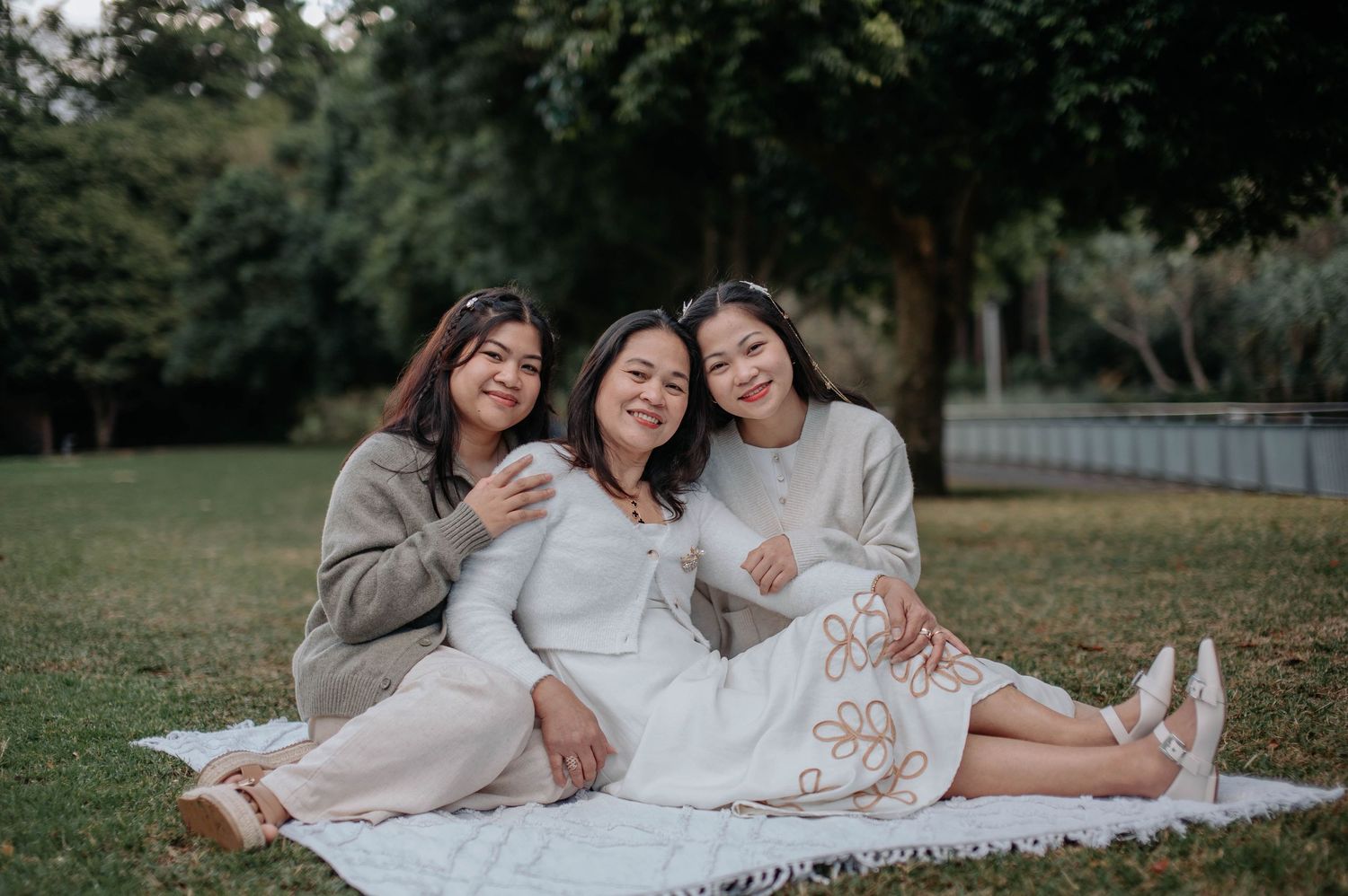 People relax on blanket while wearing coordinating white and beige outfits in outdoor garden setting.