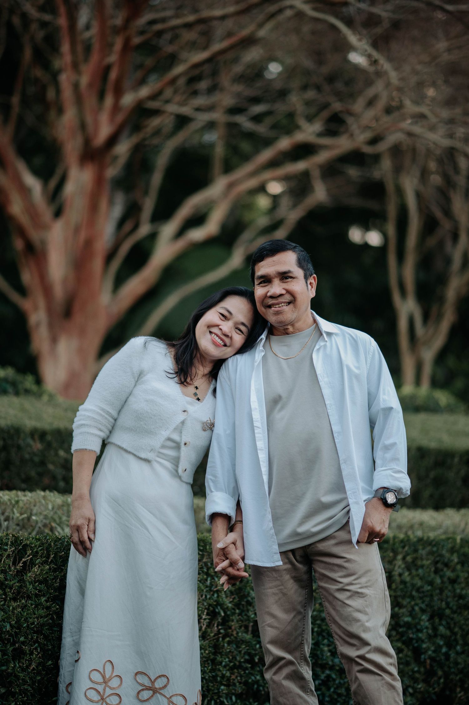 Intimate couple moment captured in casual attire against lush garden scenery with dramatic lighting.