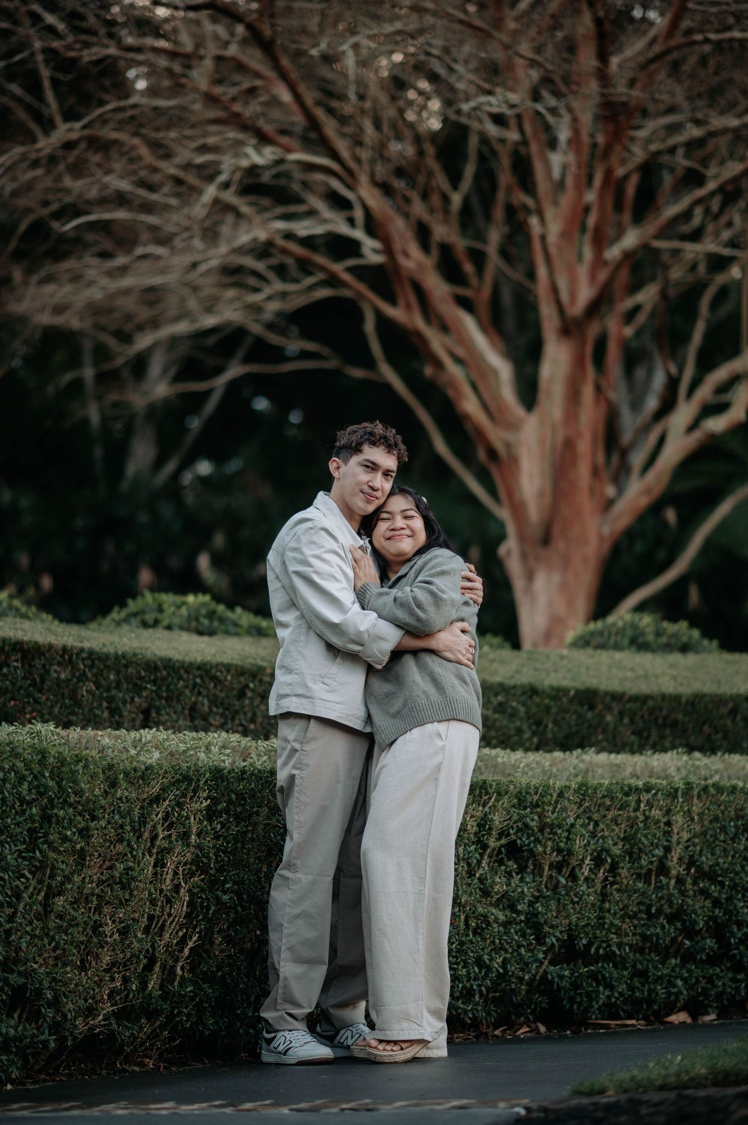 Couple shares tender moment while wearing coordinated outfits against garden backdrop.