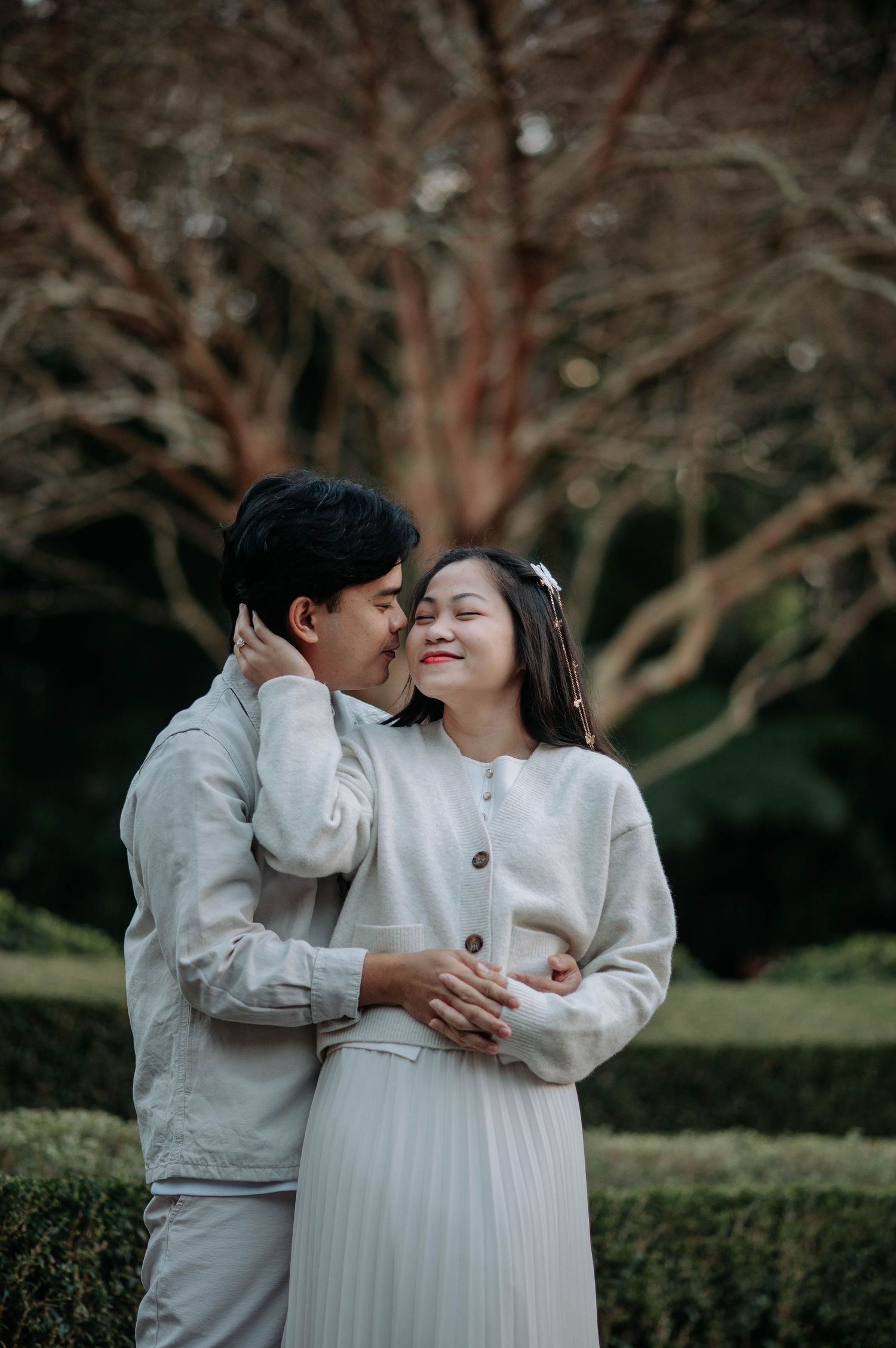 A tender moment between a couple wearing matching white outfits in a garden setting.