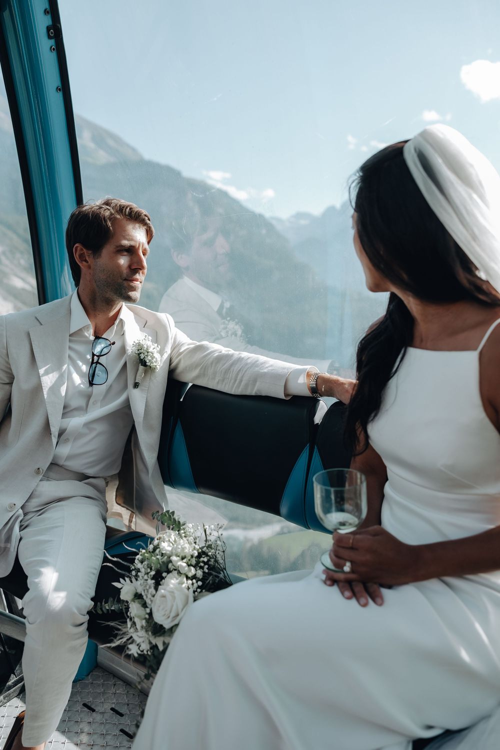 Newlyweds share an intimate moment aboard a mountain gondola with stunning alpine views in the background.
