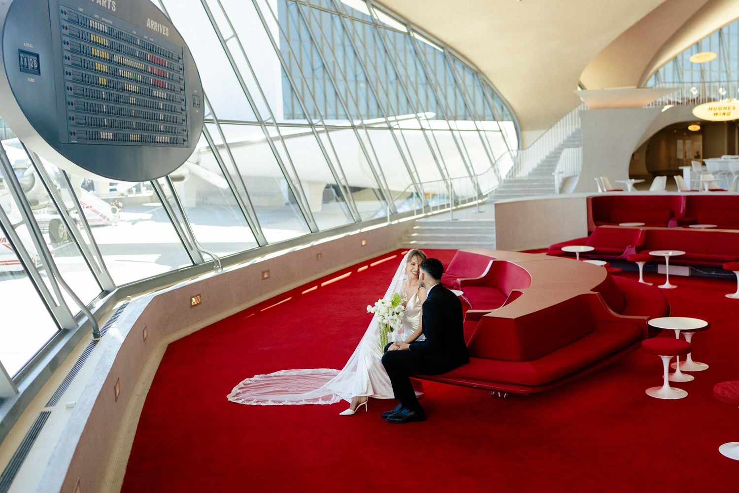 A bride and groom embrace in an elegant pose against a minimalist white architectural corner backdrop.