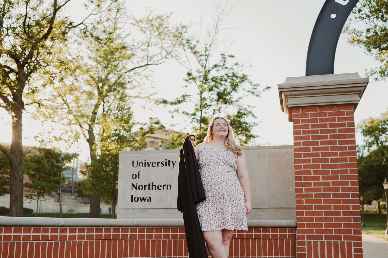 An elegant lamp post stands against a brick wall with blooming trees on a university campus during golden hour.