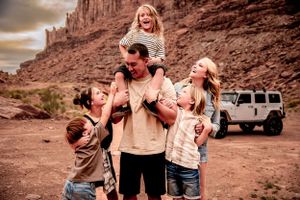 family cuddles together with son on dad shoulds and off road jeep in the background in Canonlands Moab, Utah