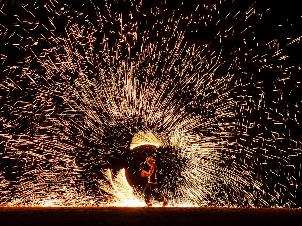 Spectaculaire pluie d'étincelles créée par un artiste du feu faisant tournoyer de la laine d'acier enflammée dans l'obscurité. Florent Vause
