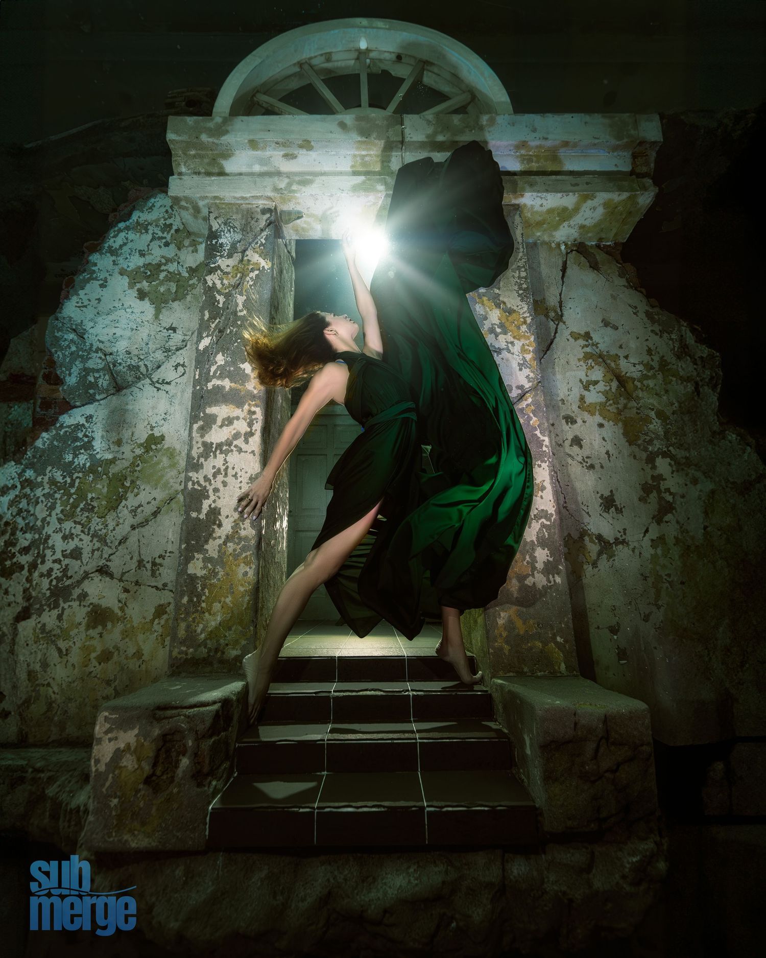 Dramatic night photo of someone in a green dress ascending old stone steps with a bright light source creating mysterious shadows.