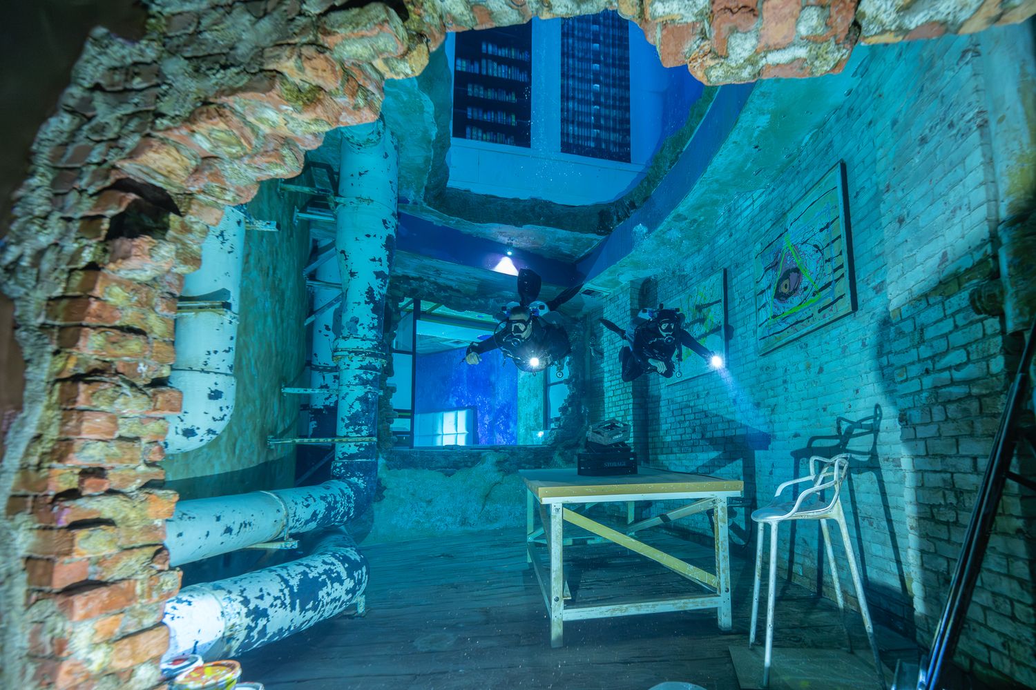 Underground corridor with blue lighting and exposed brick walls features a table and chairs in an industrial-style setting.