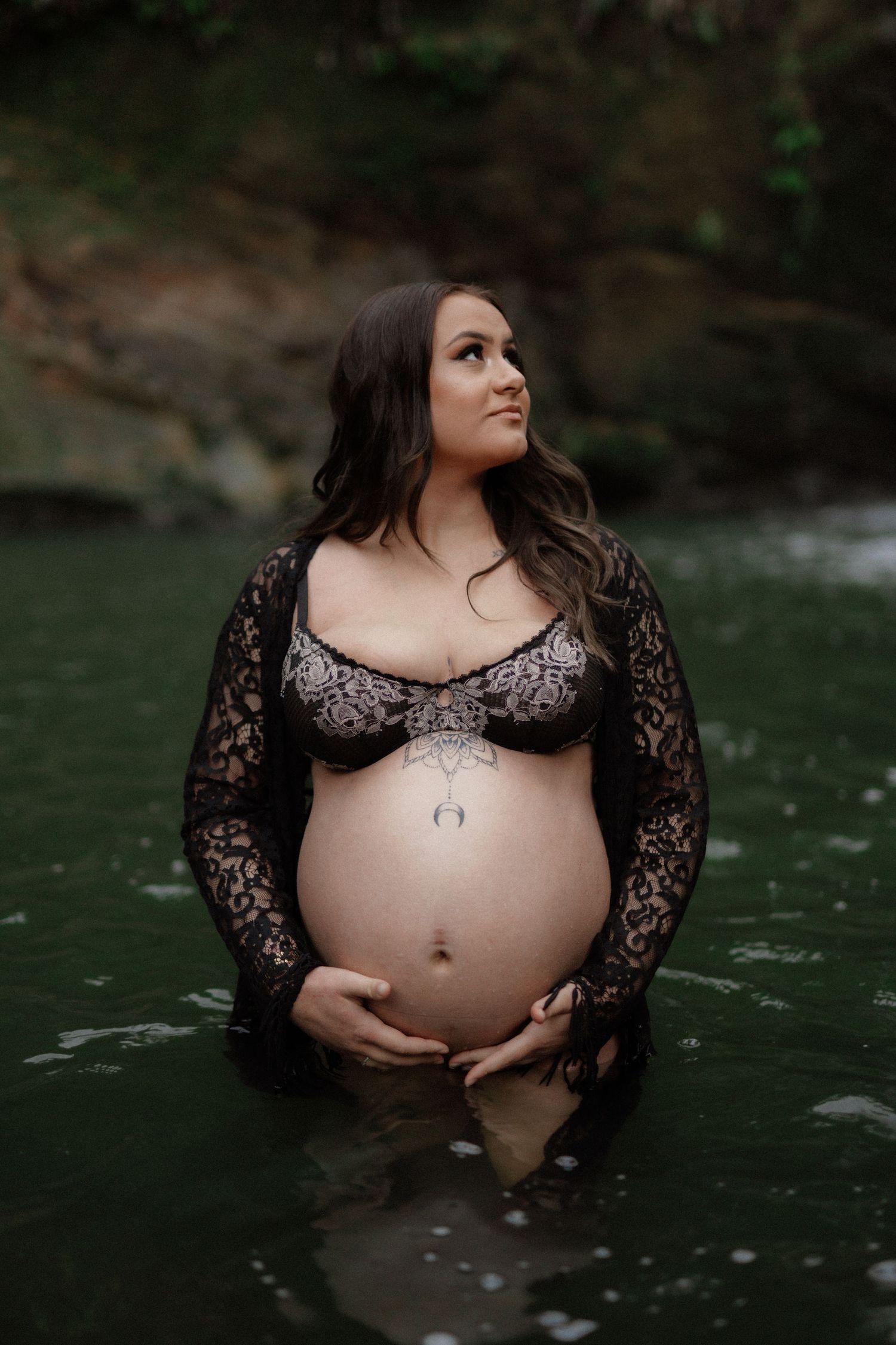 Artistic maternity photo series showing pregnant figure in black lace dress standing in dark water.