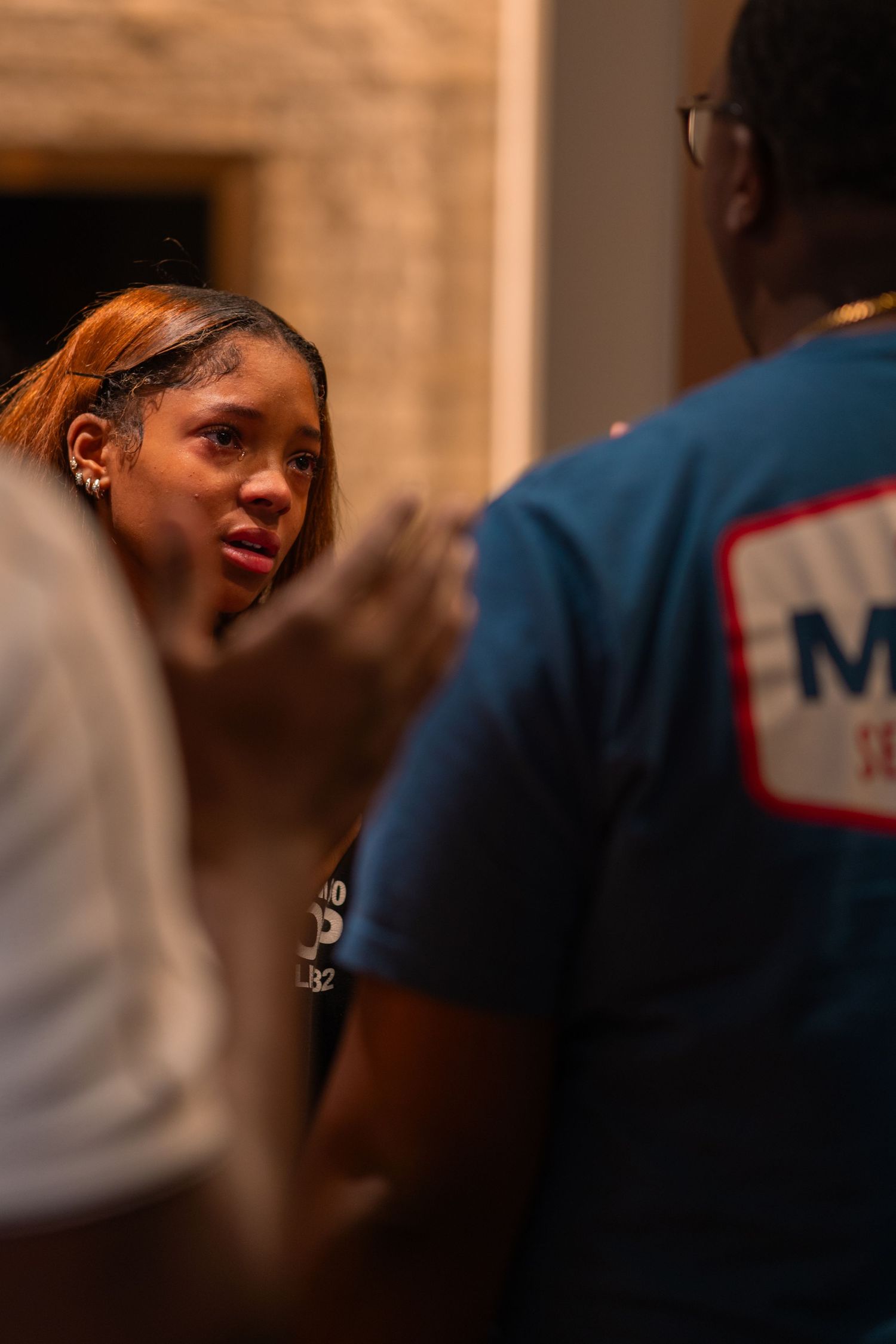 A person wearing a navy blue t-shirt works intently at a counter in a home kitchen during evening hours.