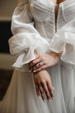 Close-up details of a white chiffon wedding dress with layered ruffles and delicate feminine hands with manicured nails.
