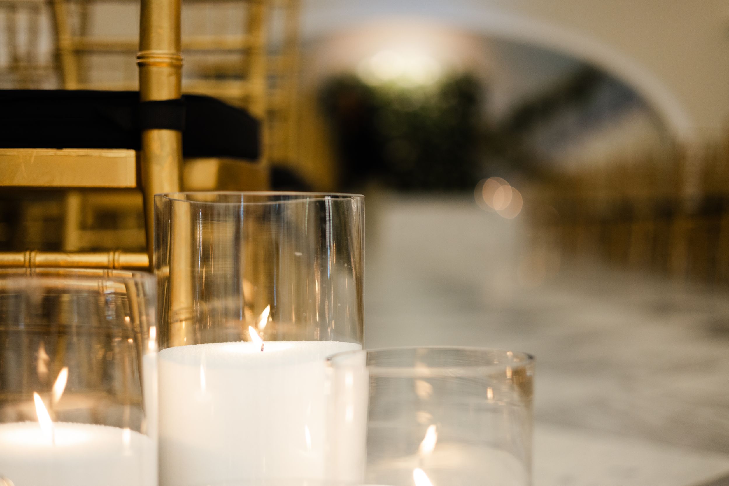 Soft candlelight glows through glass votives on an elegant table setting with a blurred background.